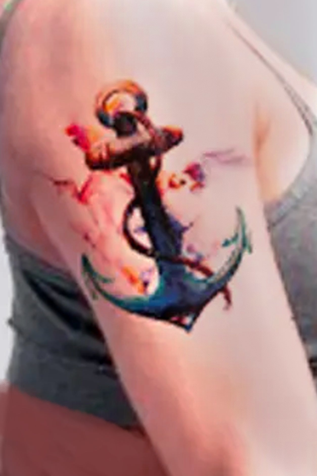 A woman wears the attractive anchor with hummingbirds on her arm. The hummingbirds are soft and colorful, moving, next to the solid anchor.