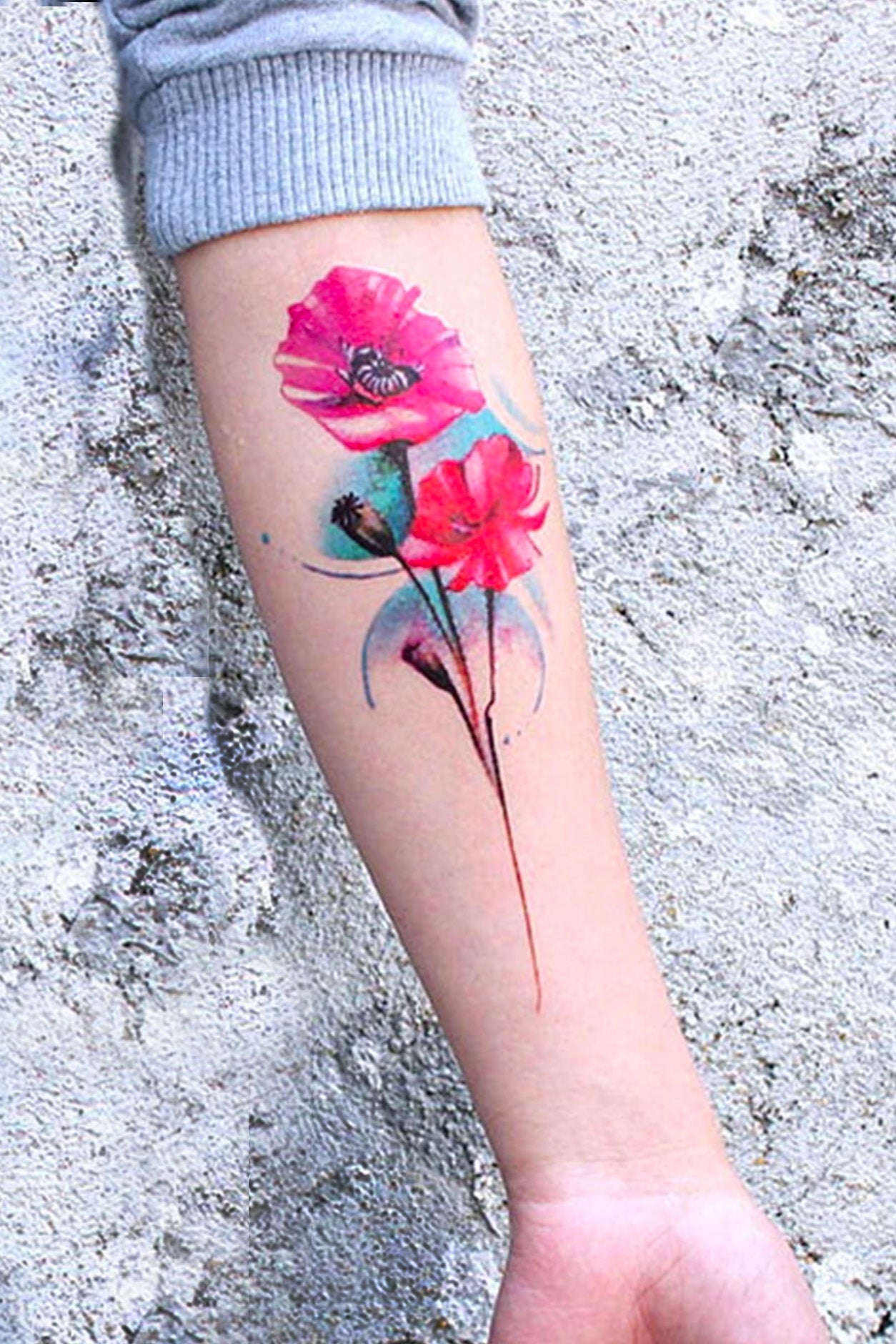 A womans arm displays the full length of the colorful double poppy tattoo in reds and teals.