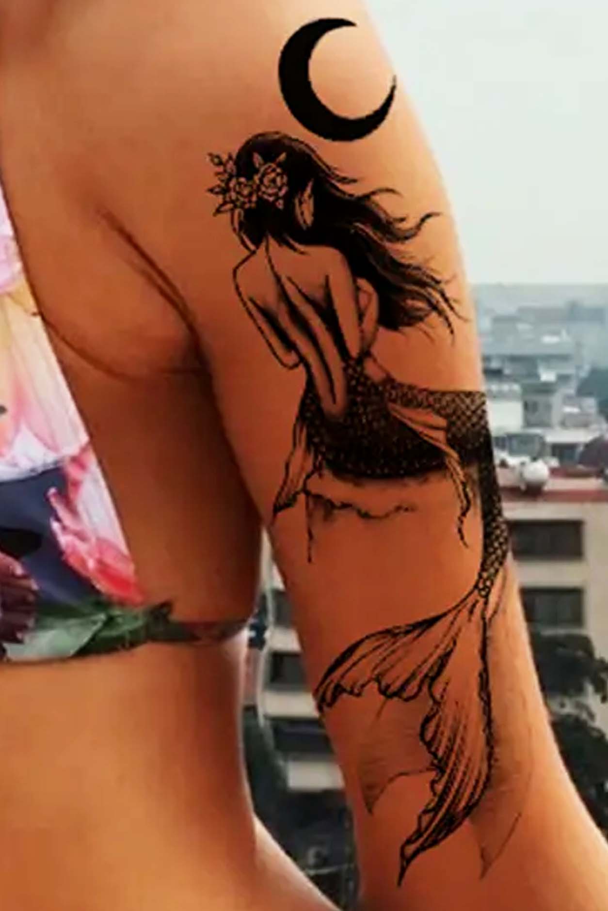A woman wears this artwork of a mermaid watching the moon from a rock. The quick tattoo is on her upper arm.