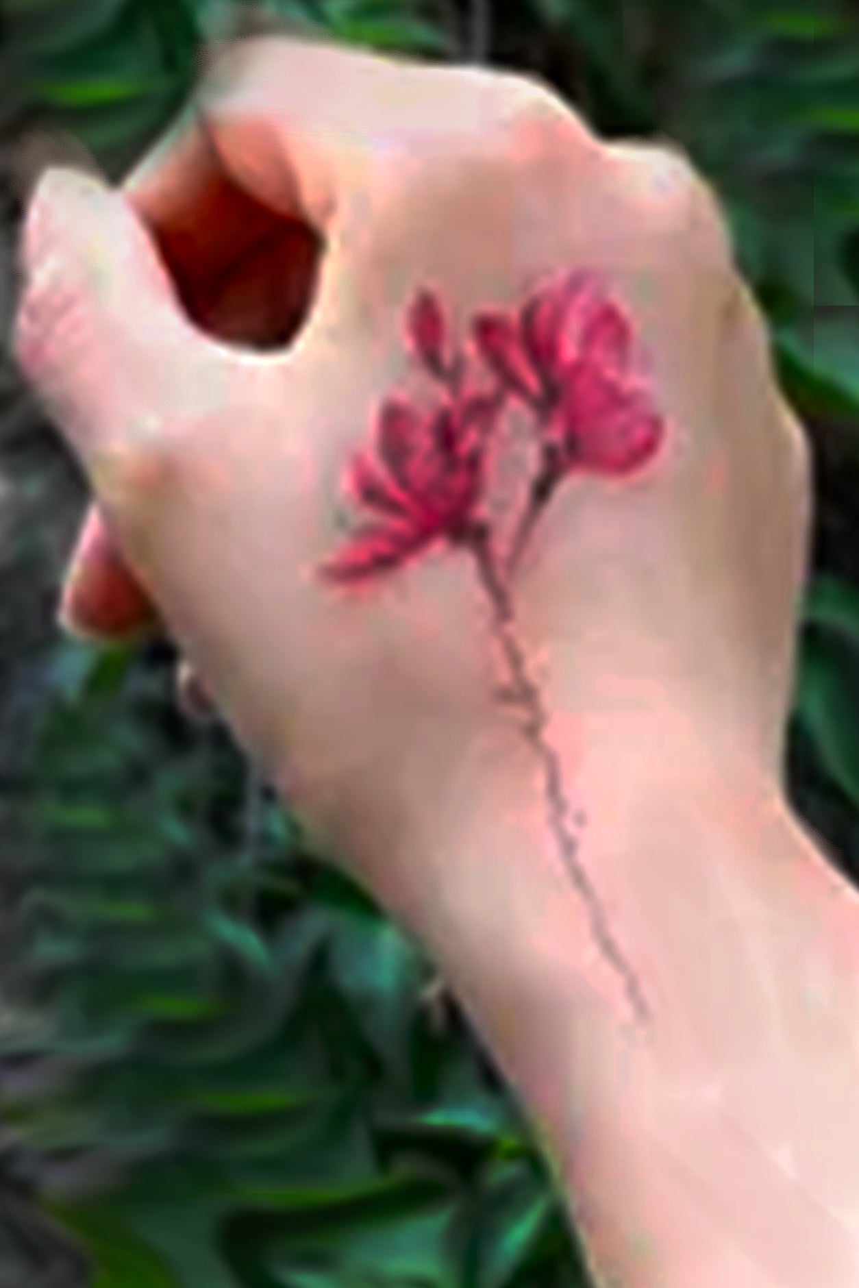 A hand displays, the smaller tattoo of the lotus buds.