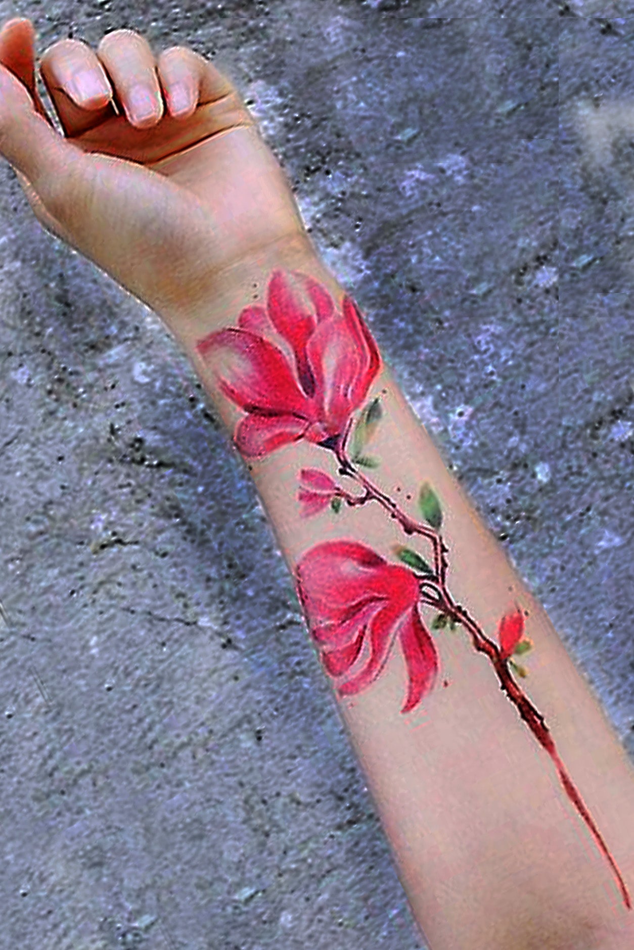 Ladies arm shows the lotus flower tattoo attached to skin, against a dark gray gravel back drop.