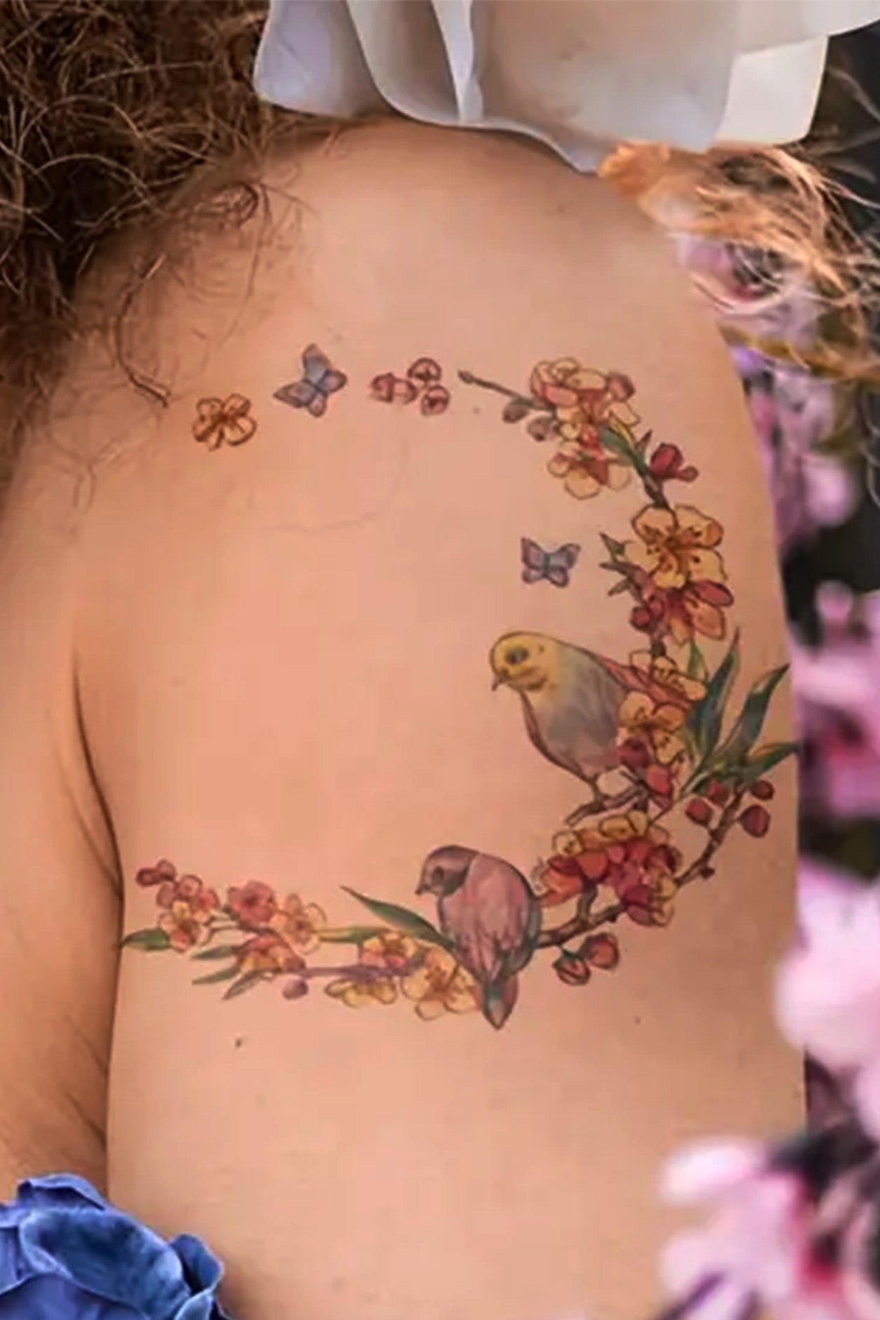 The shoulder of a young girl shows how this one semi circle of flowers and birds looks.