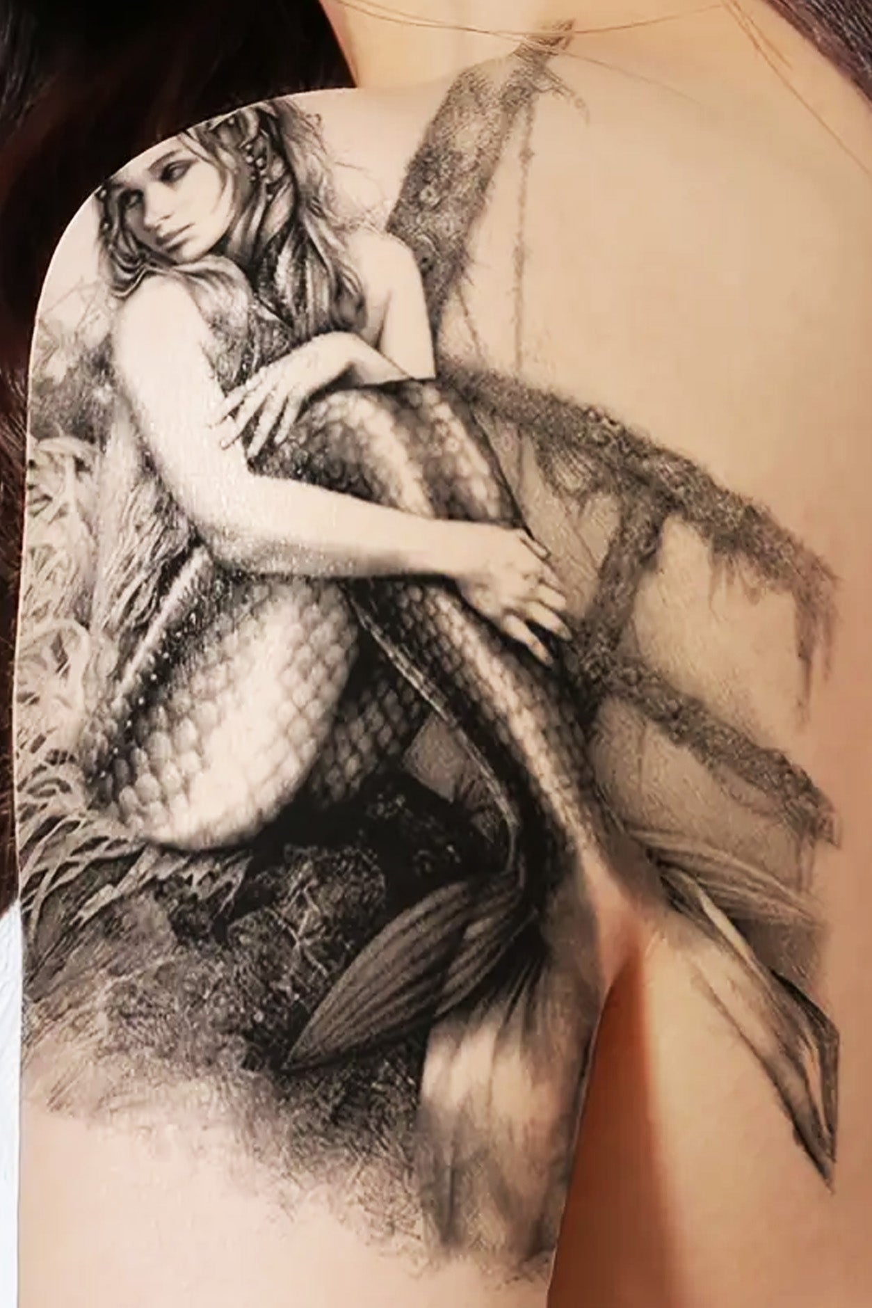 This Gender-neutral shoulder displays a beautiful mystical mermaid temporary tattoo. This highly detailed artwork is as beautiful on the skin. She has seashells in her hair, barnacles on the boat, and every scale shows in her fins.